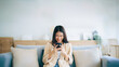 © Monster Ztudio - Happy young asian woman relax on comfortable couch at home texting messaging on smartphone, smiling girl use cellphone, chatting online message, shopping online from home