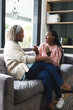 Happy african american senior mother and adult daughter sitting on couch,laughing and talking