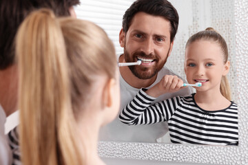 Wall Mural - Father and his daughter brushing teeth together near mirror indoors