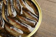 Sprats in tin can on wooden table, closeup. Space for text