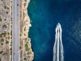 Wall Mural - Aerial overhead view of a motor boat cruising over the ocean next to a coastal highway with car traaffic