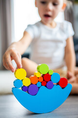 Wall Mural - Little girl playing with wooden balancing toy on the floor in home living room. Focus on balancer