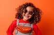 Portrait of a smiling little girl with curly hair in sunglasses on orange background