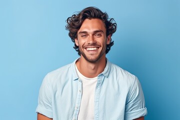 Wall Mural - Portrait of a smiling young man with curly hair looking at camera isolated over blue background