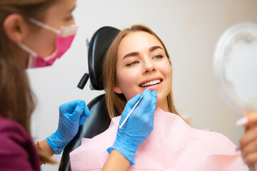 Wall Mural - Woman patient sitting in armchair during dental treatment in dental clinic. Doctor checking front teeth with instrument to check soundness of teeth