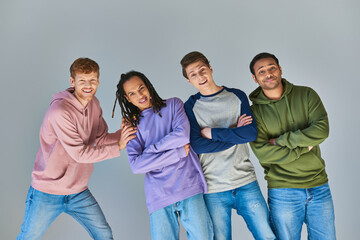 Wall Mural - four cheerful men in casual outfits smiling at camera posing on grey backdrop, cultural diversity