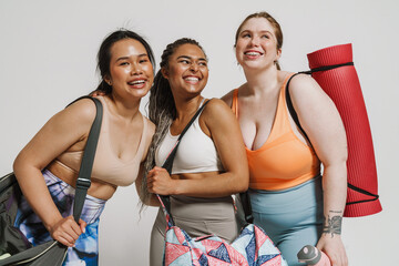 Wall Mural - Three smiling women with yoga mat posing isolated over white background