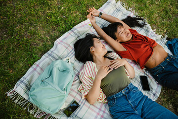 Top view of two cheerful asian women laying on blanket in park