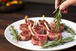 hand placing rosemary sprigs onto a dish of lamb chops