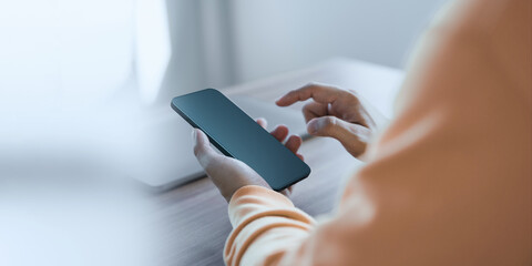 Young man holding and using a smartphone with blank desktop screen while working and drinking coffee in cafe. Mockup mobile phone.