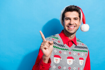 Poster - Photo portrait of handsome young guy point empty space promo dressed x-mas print vest hat outfit isolated on blue color background