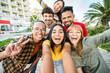 © Davide Angelini - Multiracial friends taking selfie pic with smart mobile phone outside - Happy young people having fun talking on city street - Life style concept with guys and girls hanging out on a sunny day