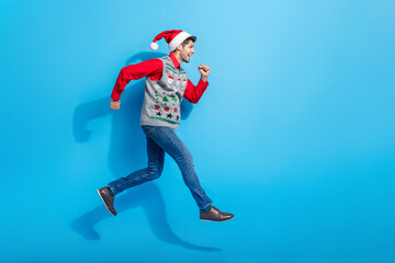 Sticker - Full body photo of cute young man jump running fast hurry dressed x-mas print vest hat clothes isolated on blue color background