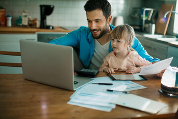 Wall Mural - Young father embracing his daughter while paying bills in the kitchen