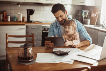 Wall Mural - Young father using the tablet with his daughter in the kitchen