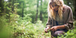 Inspiring blonde hippie woman foraging wild herbs in a cold, sparse forest.