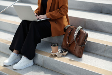 Wall Mural - Cropped shot of young stylish female digital nomad typing on laptop keyboard while sitting on grey concrete staircase in front of camera