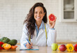 Portrait of cheerful female dietologist holding grapefruit, recommending fresh food, working at clinic