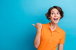 © deagreez - Photo of cheerful impressed girl dressed orange polo looking pointing thumb empty space isolated blue color background