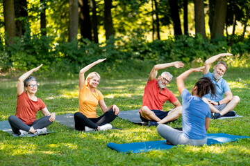 Sporty mature people doing stretching exercises during group training with instructor outdoors