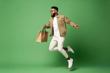 Wall Mural - Excited young man jumping with shopping bags on green background in studio with copyspace, for banner background