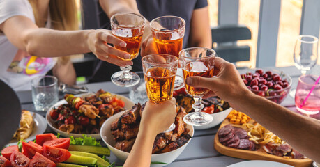 Vegetables and meat are grilled on the table with wine and people. Selective focus.