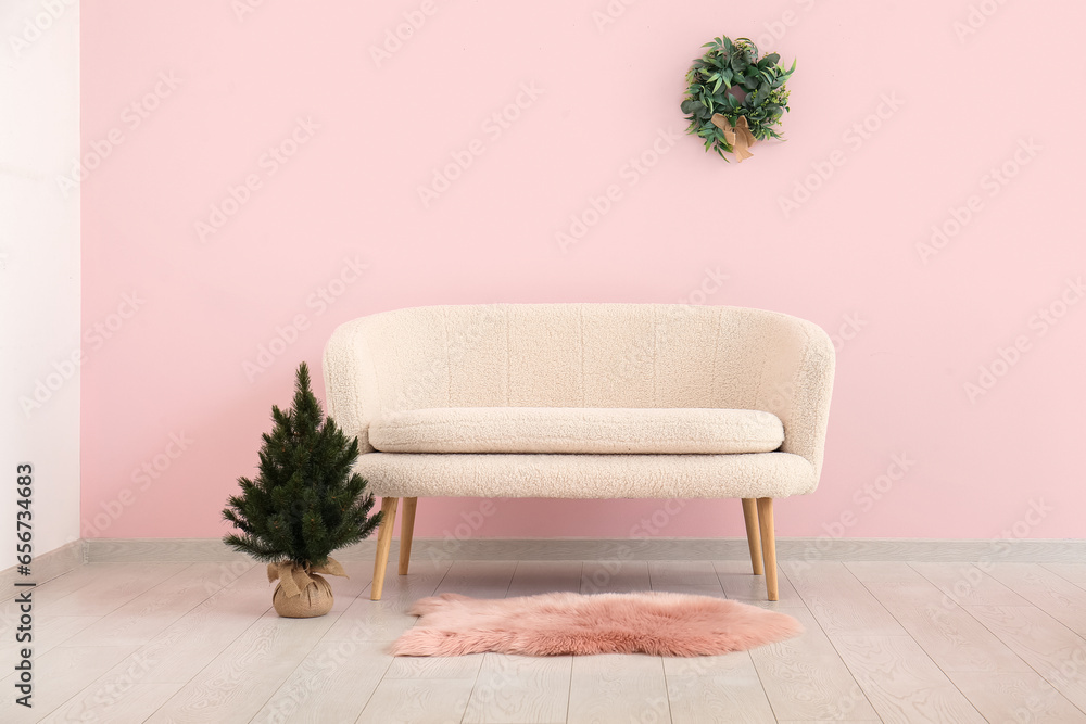 White sofa and small Christmas tree near pink wall