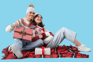 Wall Mural - Happy young couple in warm clothes with gift boxes sitting on blue background