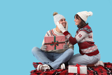 Wall Mural - Happy young couple in warm clothes with gift boxes sitting on blue background