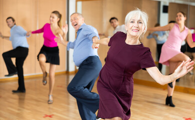 Wall Mural - Portrait of positive older woman enjoying active dancing during group training in dance studio..