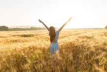 Girl With Long Hair Stretching Arms Amidst Wheat Crop In Field