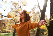 Autumn Leaves Falling On Redhead Woman With Arms Outstretched At Park