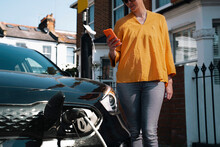 Woman using smart phone standing near electric car