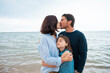 © Westend61 - Father and mother kissing each other with daughter in front of sea