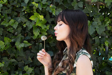 Young Woman Blowing On Dandelion Flower