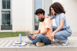© Westend61 - Smiling students using laptop on concrete bench in campus