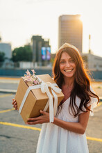 Happy woman holding gift box at sunset