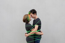 Teenage Couple Tied Up With Green Rope Embracing Each Other Against Gray Background