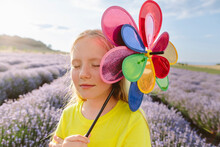 Smiling Girl With Eyes Closed Holding Pinwheel Toy In Lavender Field