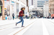 © Westend61 - Young woman wearing headphones and crossing street in city