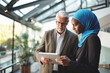 © SnapVault - A Muslim secretary displays information on a tablet to her boss in an office environment. Multicultural diversity in workplace environments concept.