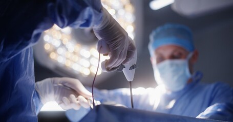 Adult male surgeon looks at monitor and operates patient with his colleagues. Professional medics use modern laparoscopy instruments during surgery in operating room. Medical staff at work in clinic.