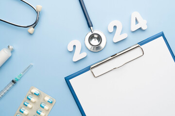 Wall Mural - 2024 Happy New Year banner for health care and medical concept. Stethoscope with doctor order chart, prescription, pills, syringe, vaccine vial and white number 2024 on table blue background.