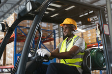 African American Male Warehouse Worker In Safety Vest And Helmet Driving And Operating On Forklift Truck For Transfer Products Or Parcel Goods In The Industrial Storage Warehouse