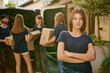 © master1305 - Focus on girl, volunteer standing outdoors near van on sunny day. Young people on background loading boxes into van. Concept of humanitarian aid, assistance and support, care, social programs