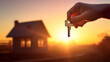 © ND STOCK - An image of a woman holding a key and a wooden house silhouette against the sun. Home ownership concept, real estate concept