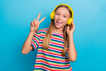 Poster - Portrait of good mood positive teen girl wear colorful t-shirt in headphones showing v-sign symbol isolated on blue color background