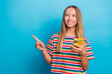 Sticker - Portrait of small little girl wear colorful t-shirt browsing smartphone look directing empty space isolated on blue color background