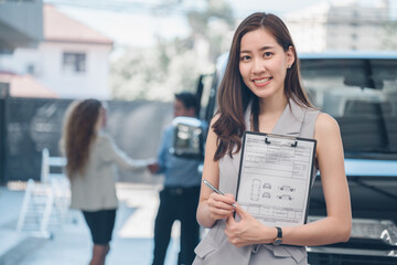 Portrait of professional female salesperson at car dealership. Posing proudly at auto showroom, smiling to the camera. Happy saleswoman Asia working at automobile, background customer and car.