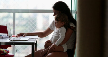 Wall Mural - Candid toddler boy on mother lap watching video on computer laptop at home